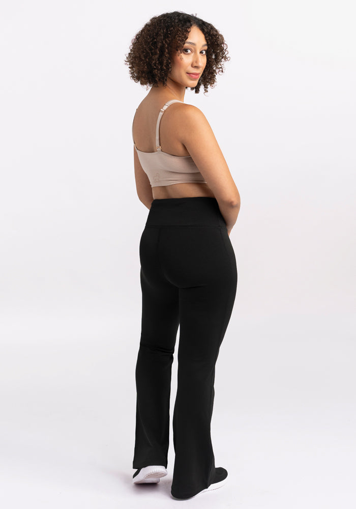 A person with curly hair stands facing away, glancing over their shoulder. They are wearing a beige top paired with Woolx's Marissa Pants in black against a plain white backdrop.