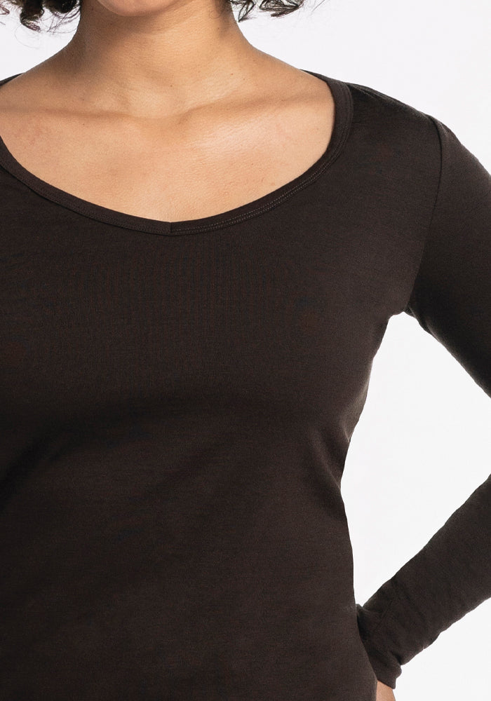 A person is wearing the Layla V Neck Top in French Roast by Woolx, shown from neck to waist. The top features long sleeves and a scoop neckline. The background is plain white.