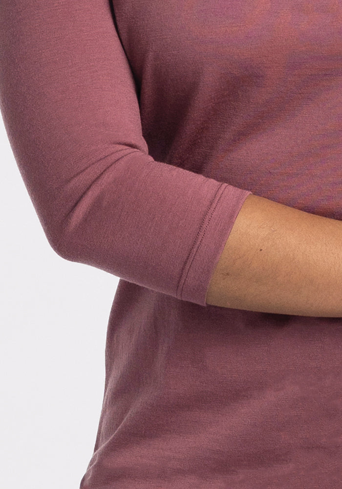 A close-up shot showcases a person wearing the Woolx Jenny 3/4 Sleeve Crew Neck in Wild Ginger, with their elbow bent against a white background. This top is made from lightweight Merino wool.