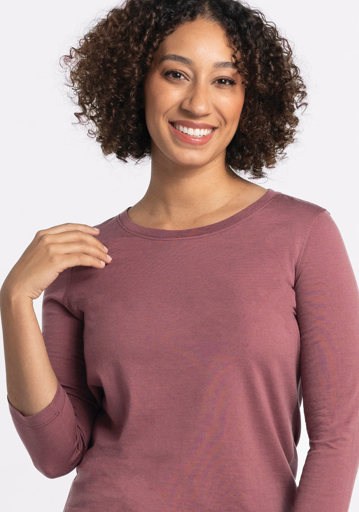 A person with curly hair is smiling, wearing the Woolx Jenny 3/4 Sleeve Crew Neck in Wild Ginger, set against a plain white background.