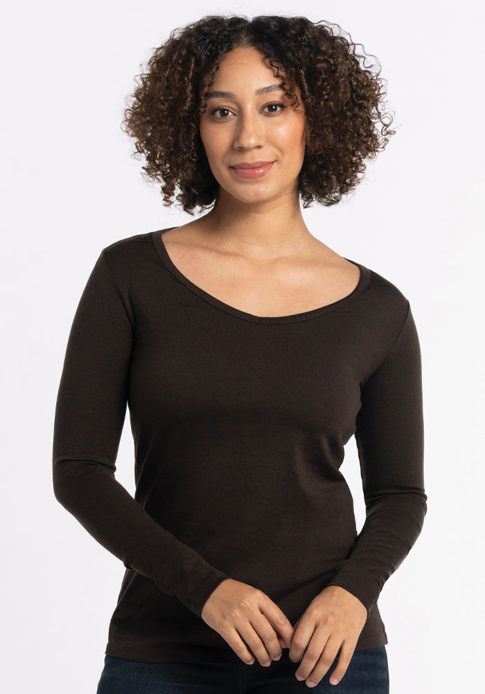 A person with curly hair is wearing the Woolx Layla V Neck Top in French Roast, a long-sleeve breezy knit shirt. They stand against a plain white background with a neutral expression. 