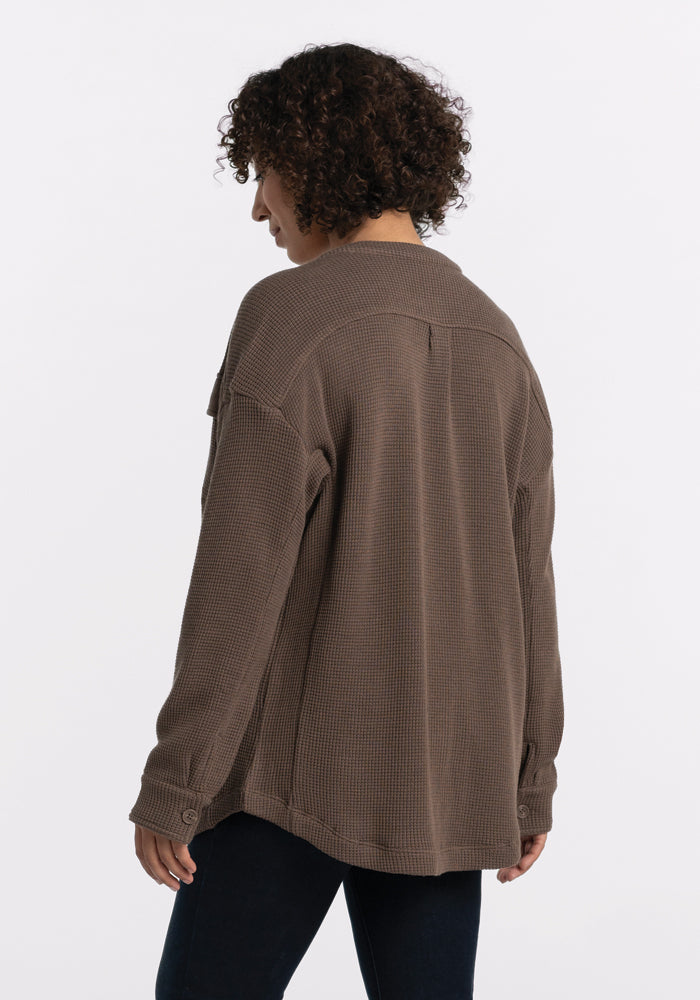 A person with curly hair is dressed in the Oaklynn Waffle Shacket - Latte from Woolx, shown from behind. They are positioned against a plain white background, highlighting a neutral tone that enhances the shacket's textured fabric.