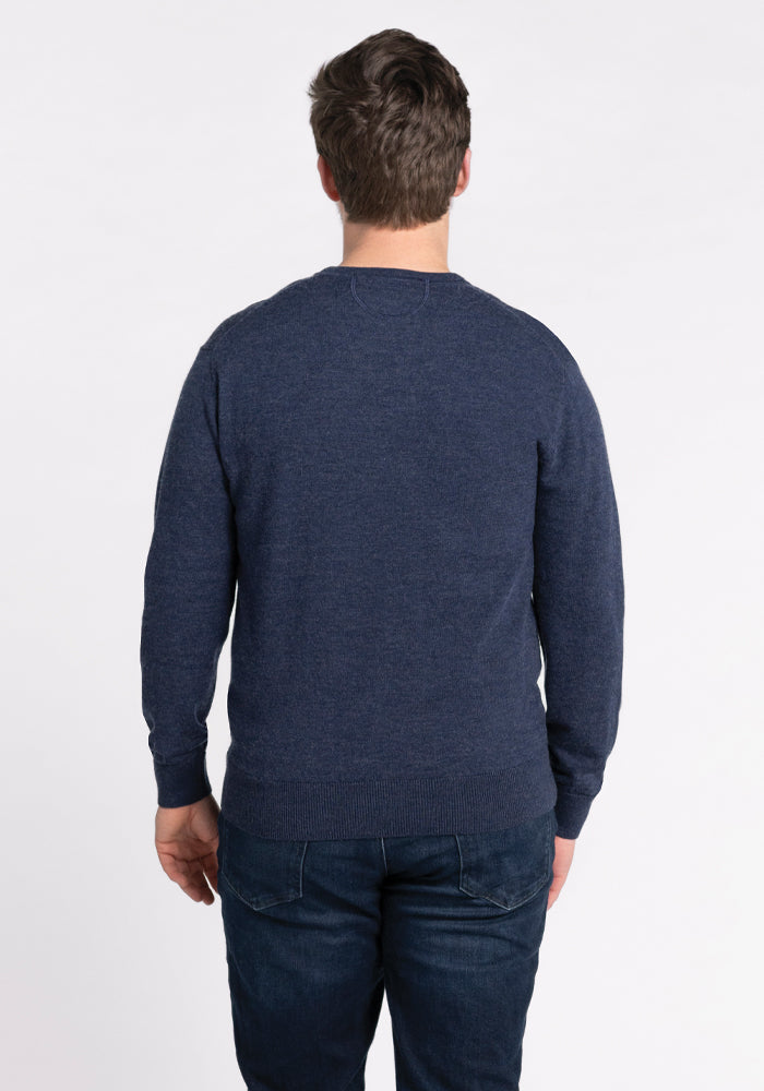 A person is facing away from the camera, wearing a Woolx Vincenzo Sweater in Twilight Storm and dark jeans, set against a plain white background.