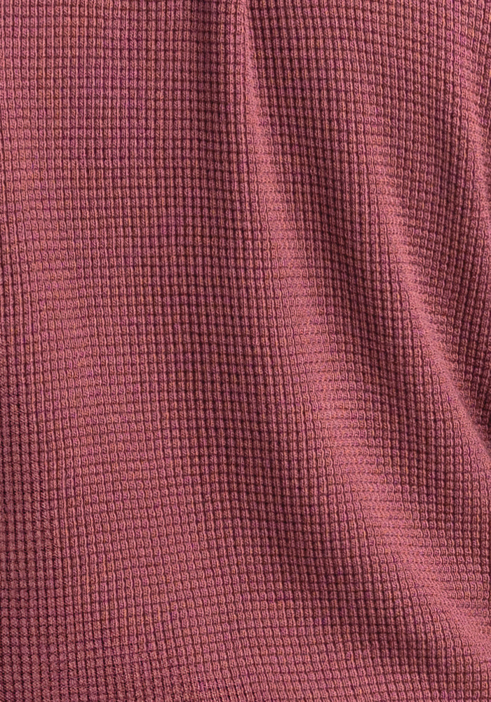 Close-up of the Oaklynn Waffle Shacket by Woolx, showcasing a textured fabric in a rich wild ginger hue with a waffle-like pattern. The material, reminiscent of merino wool, looks soft and slightly draped, casting gentle shadows and highlights across its surface.