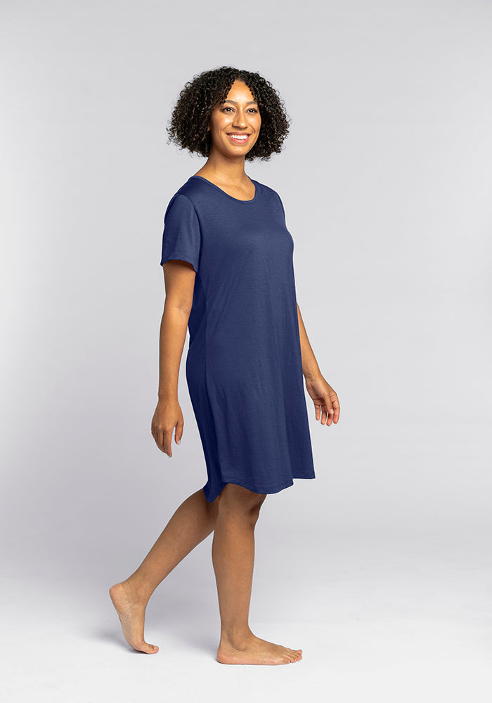 A person with curly hair, wearing the Desi Nightgown - Starry Night by Woolx, smiles while walking barefoot against a plain gray background.