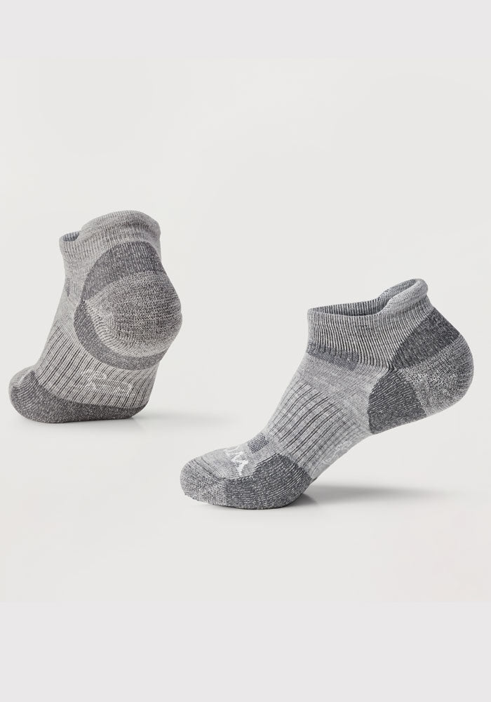 Displayed against a plain background is a pair of Rowan No Show Tab Lightweight Socks in grey, crafted by Woolx. Made from Merino wool, they feature ribbed cuffs, cushioned soles, and darker heel and toe sections. One sock stands upright while the other leans back, highlighting their shape and antimicrobial properties.