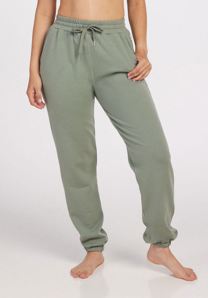 A person stands barefoot against a plain background, wearing mint Parker Sweatpants by Woolx. One hand rests in a pocket, and the Merino wool pants feature an elastic waistband with a drawstring and cuffed ankles, offering temperature-regulating comfort.