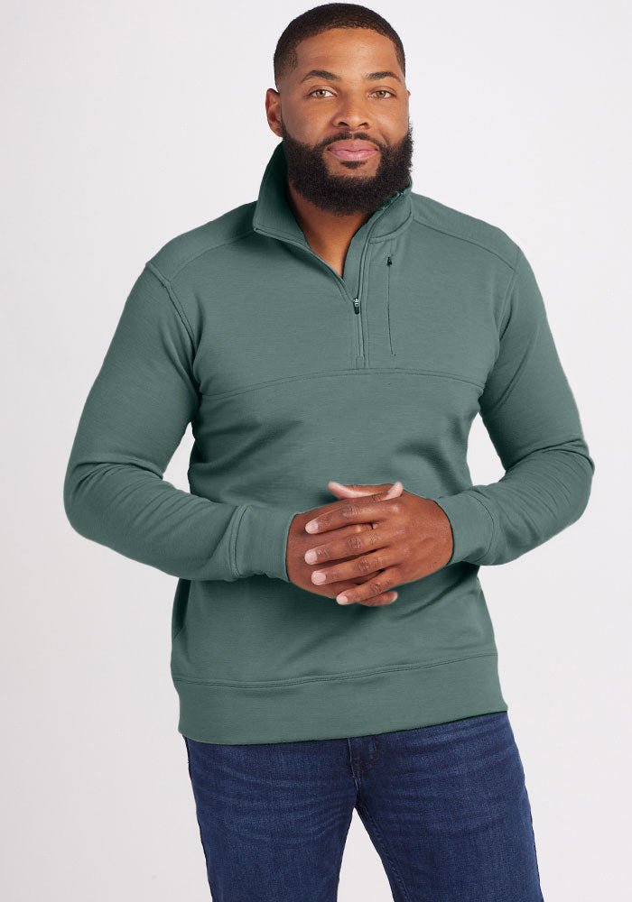 A man with a beard is wearing the Wool Aire™ Mason pullover in Duck Green from Woolx, paired with blue jeans. He stands against a plain white background with hands clasped in front of him, looking directly at the camera.