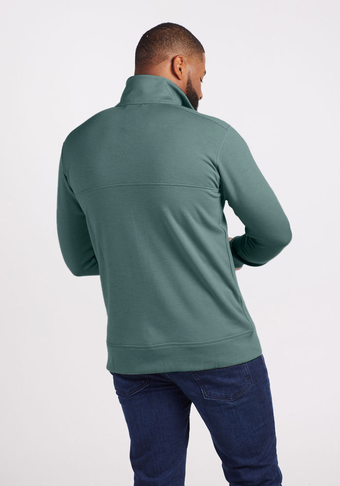 A man stands with his back to the camera, displaying the Woolx Wool Aire™ Mason jacket in Duck Green. Its high collar and seam across the upper back lend a refined touch, perfectly paired with dark jeans against a plain white background.