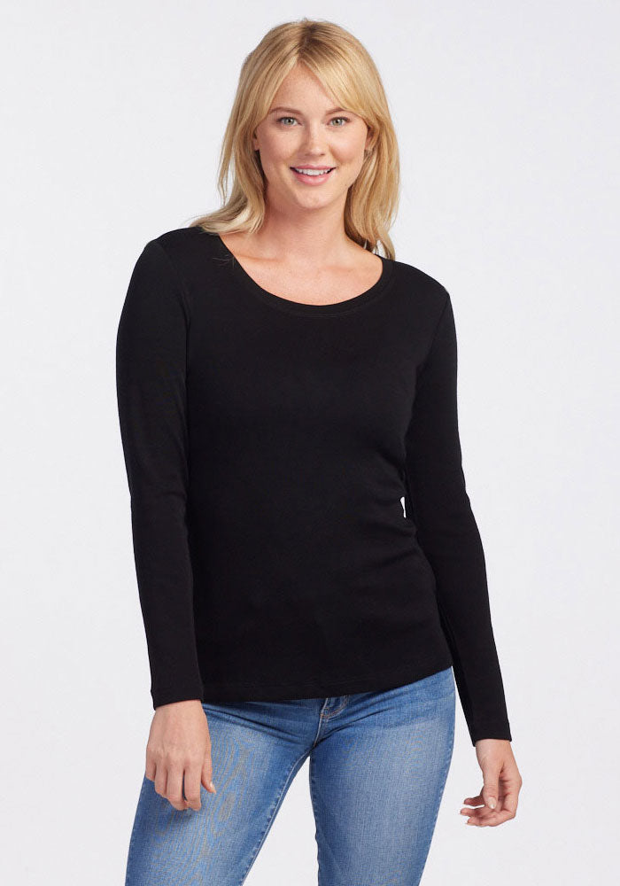 A person with blonde hair is wearing a black Woolx Kenzie Scoop Neck, celebrated for its warmth and comfort, paired with blue jeans. They are smiling against a plain light background.