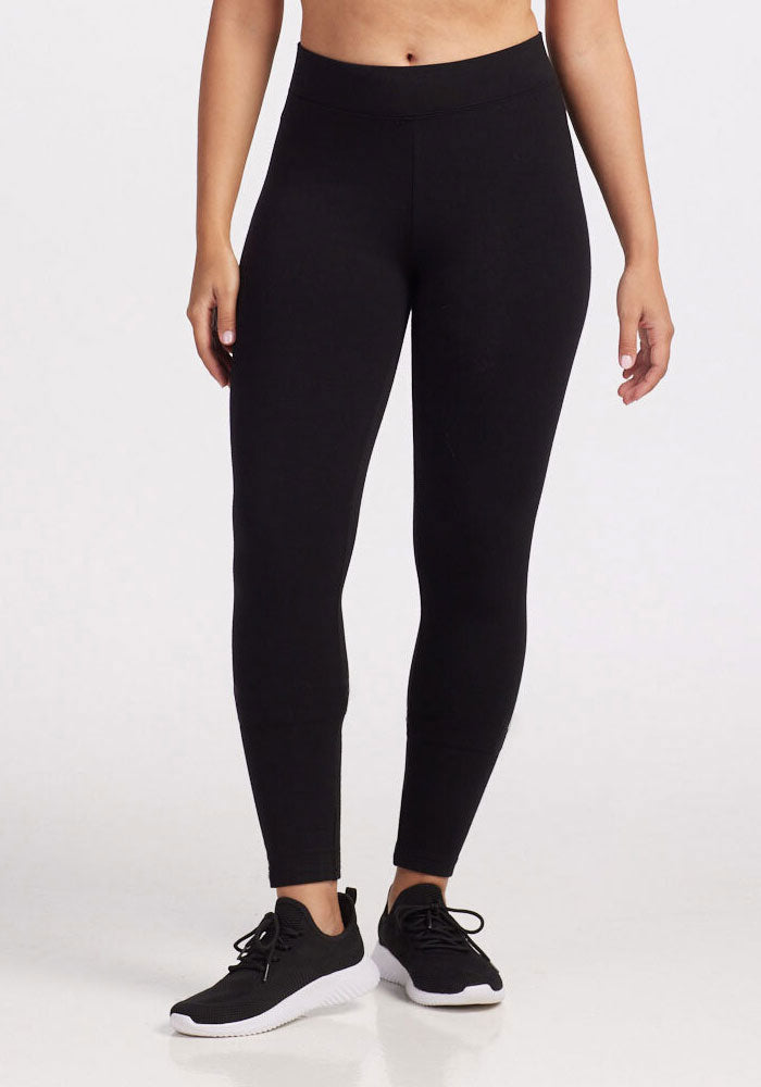 A person wearing Woolx's Stella Leggings in black along with black sneakers stands against a plain white backdrop. The outfit is casual and athletic, ideal for exercise or leisure activities during the chilly months.