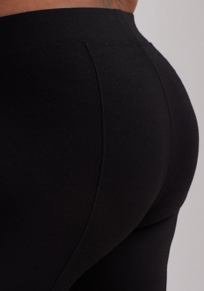 A close-up image of a person wearing tight black Stella Leggings from Woolx, showing their lower back and buttocks. The material appears to be stretchy and fits snugly, emphasizing the contours of the body. The background is plain and neutral.