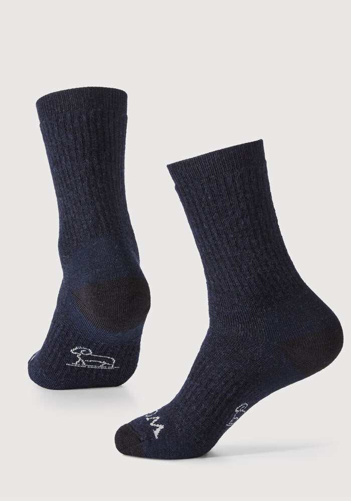 A pair of Woolx's Core Crew Sock Full Cushion in navy, crafted from moisture-wicking Merino fabric, is displayed against a light background. The socks feature white logos on the soles and are shown from various angles to emphasize their texture and design.