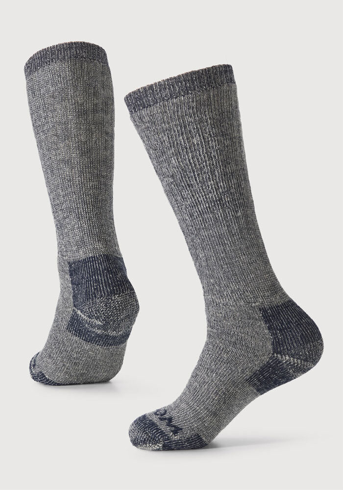 Two navy carbon Extreme Full Cushion Over The Calf Socks by Woolx are displayed against a plain background. They feature reinforced darker gray heels and toes, ribbed cuffs, and offer moisture-wicking odor-resistant properties. The socks are angled to show both front and back details for clarity.