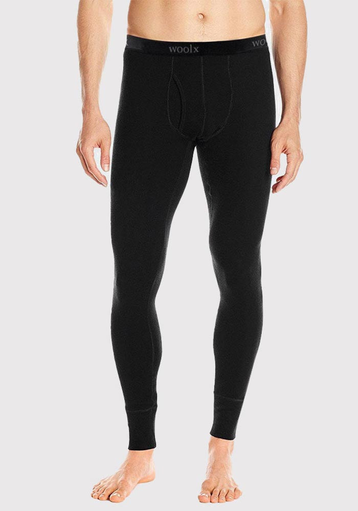 A person is wearing black Woolx Arctic Leggings made from Merino Wool. The Ultra-Heavyweight thermal leggings reach down to the ankles and have a fitted, form-hugging design. The waistband is slightly elastic with the brand "Woolx" visible. The person is standing barefoot against a plain background.