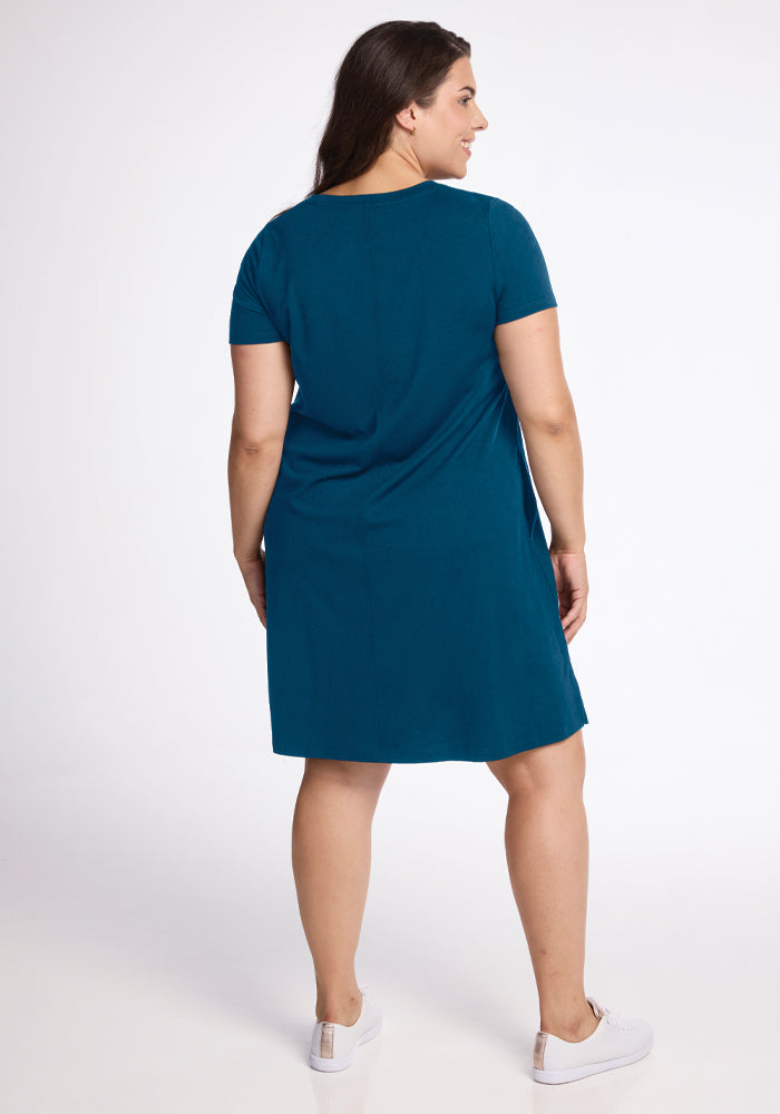 A person with long dark hair is wearing the Georgie Dress in Real Teal from Woolx and white sneakers, standing with their back to the camera against a plain white background.