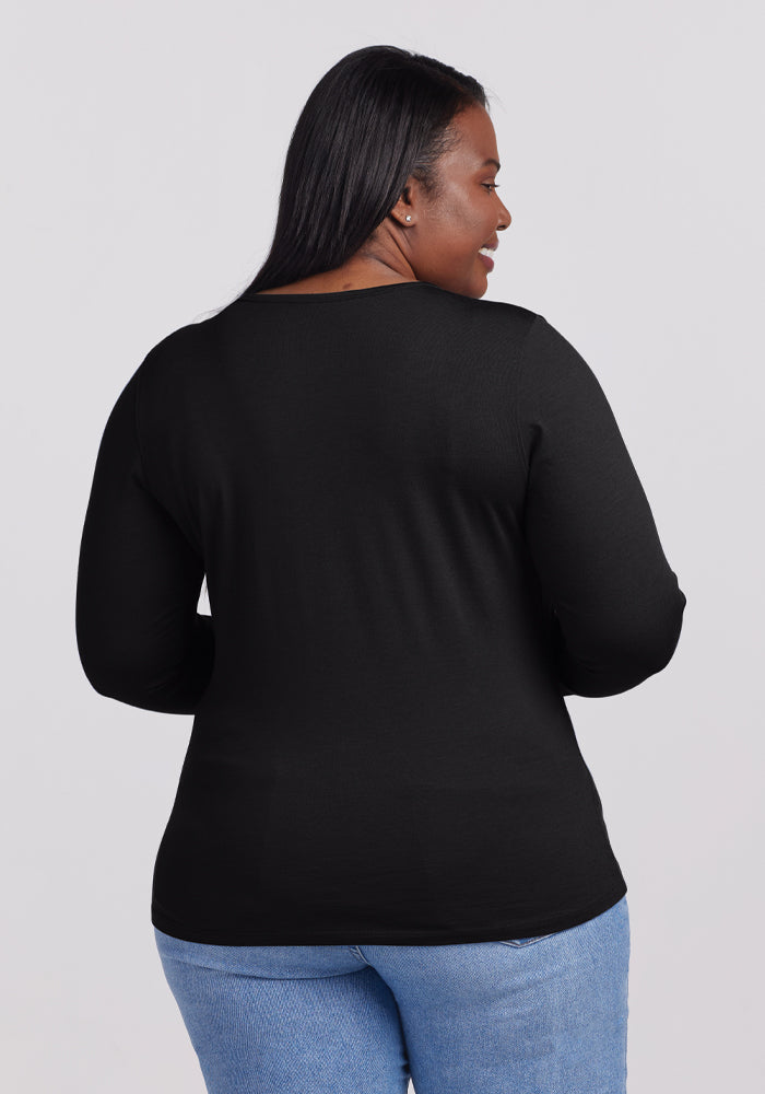 A person with long hair faces away, wearing the sleek black Remi Long Sleeve T-Shirt by Woolx, known for its odor-resistant Merino wool, paired with blue jeans against a plain white background.