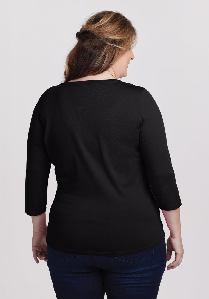 A woman with long hair stands facing away, wearing the Woolx Jenny 3/4 Sleeve Crew Neck in black and dark jeans against a plain white background, showcasing this versatile wardrobe staple's timeless elegance.