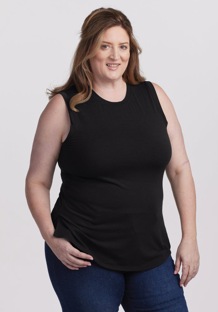 A person with long hair in a classic Bella Tunic Top - Black by Woolx and blue jeans smiles against a plain white background, truly embodying a timeless summer staple. 