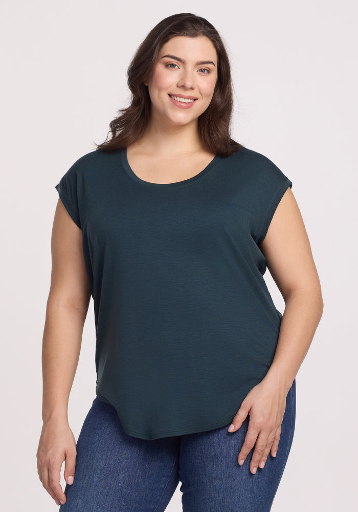 A woman with long dark hair smiles wearing the Woolx Gabi Tunic Top in Enchanted Forest, a versatile dark green, short-sleeve piece made from Australian Merino Wool, paired with jeans against a plain white background. 