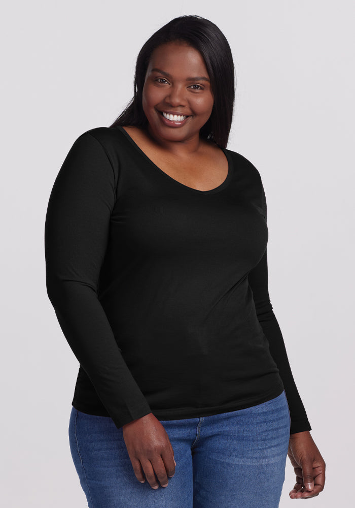 A person in a Woolx Layla V Neck Top - Black, crafted from odor-resistant merino wool, effortlessly pairs it with jeans against a plain grey background, showcasing both style and functionality. 