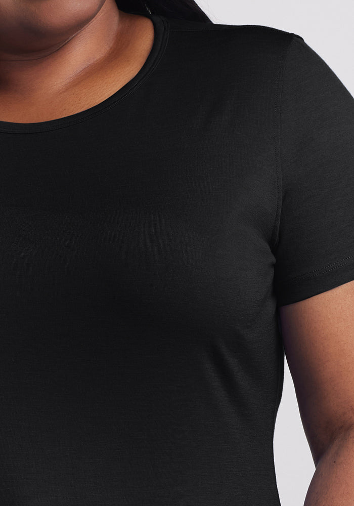 Close-up of a person wearing the Woolx Liza Crew Neck Tee - Black, made from moisture-wicking fabric. The image highlights the upper torso with a focus on the sleeve and shoulder against a light gray backdrop.