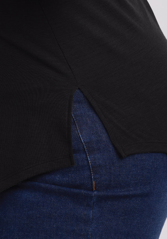 Close-up of a person in Woolx's Bella Tunic Top - Black paired with blue jeans. The top, featuring a side slit, showcases the texture interplay, emphasizing color contrast and making it an ideal summer clothing choice.