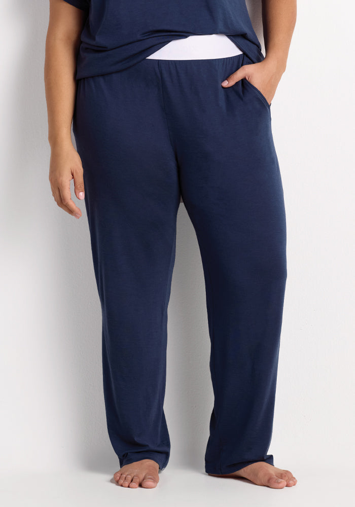 A person wearing the Maya Lounge Pants - Starry Night from Woolx stands barefoot, one hand in their pocket against a plain white background; these loose-fitting pants are made from odor-resistant Merino wool and are ideal for travel comfort. 