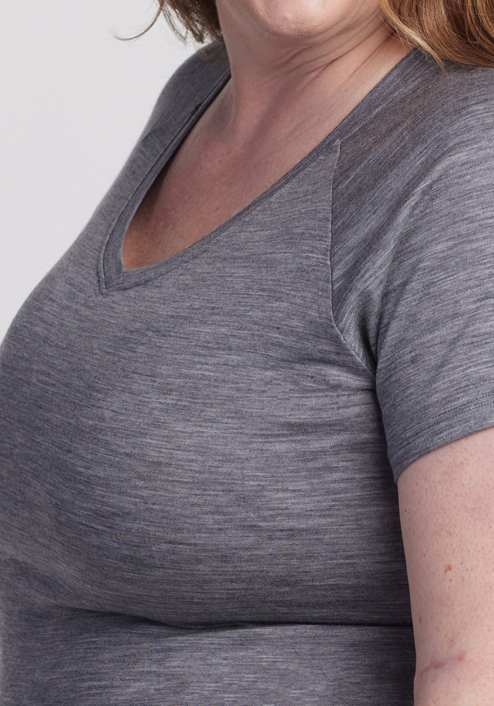 A person is shown from the shoulders down wearing a Woolx Mia V Neck in Graphite Heather, appearing soft and slightly textured. Made from comfortable merino wool, this tee stands out against the plain white background.