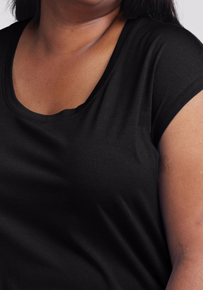 The person is wearing the Woolx Gabi Tunic Top in black. The close-up image highlights the fabric texture on their upper torso and shoulder, with a blurred background accentuating the tunic's versatility.