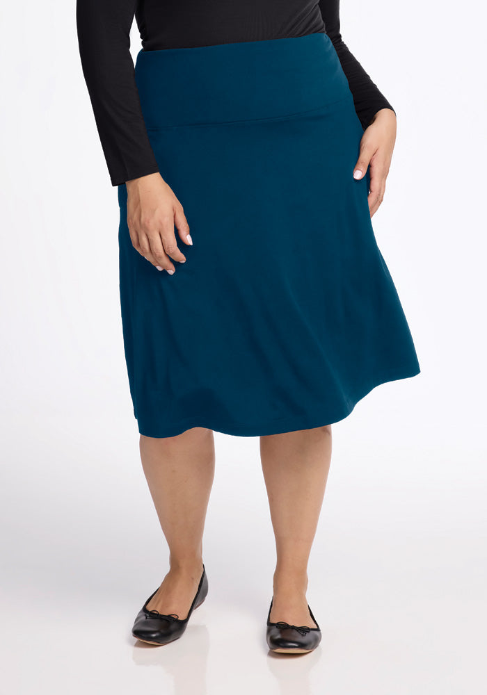 A person wearing a black long-sleeve top and the Marilyn Flowy Midi Skirt in Real Teal from Woolx stands on a white background. They are wearing black flat shoes with bows. The focus is on the clothing.