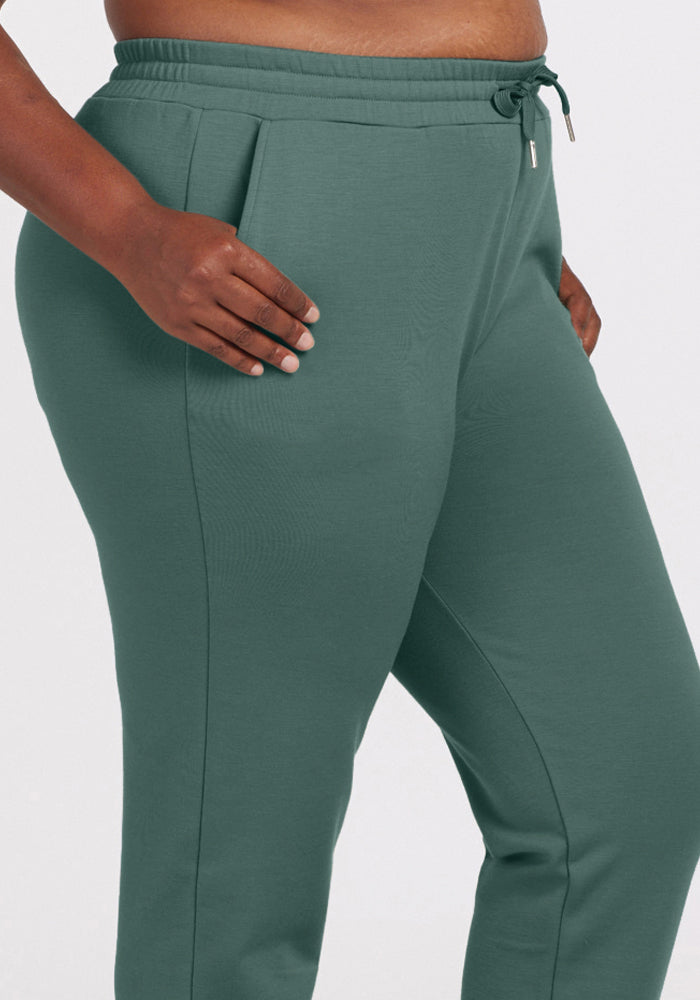 A person wearing duck green Parker Sweatpants from Woolx, featuring a drawstring waistband. Made of a soft Merino wool blend, these pants include convenient pockets. The person stands with one hand resting on their hip against a plain white background.