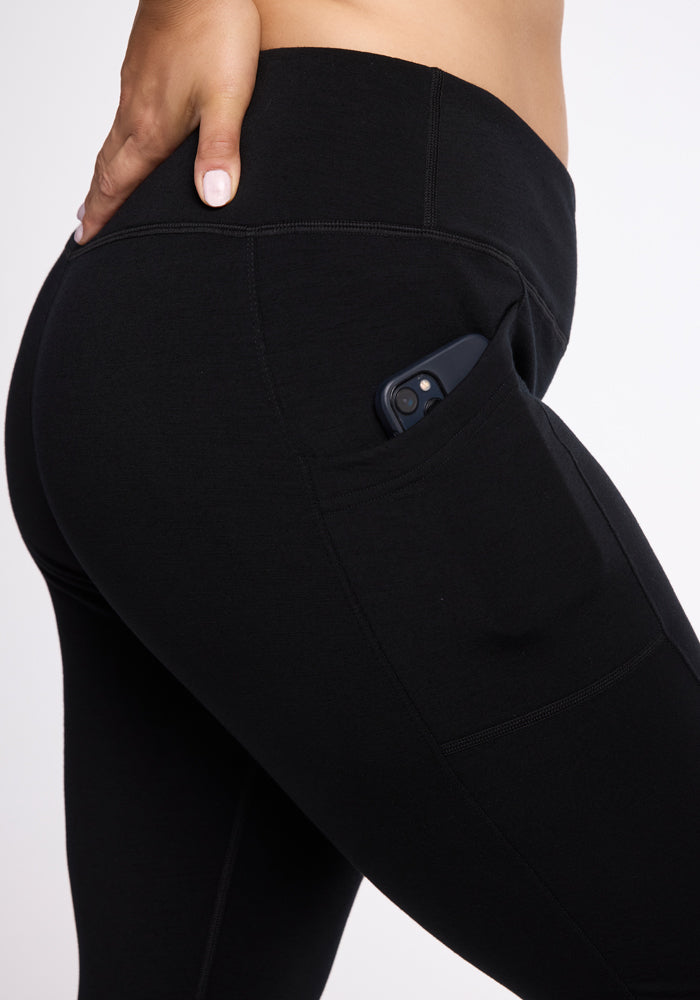 Close-up of a person wearing Woolx Frost Duralite® Leggings - Black with their hand resting on the hip. A smartphone is partially visible in the pocket on the side of these warmest leggings.